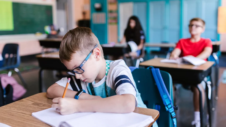 Junge in Klassenraum an Tisch schreibt