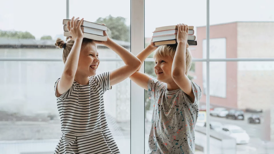 Junge und Mädchen mit Büchern über dem Kopf vor Fenster